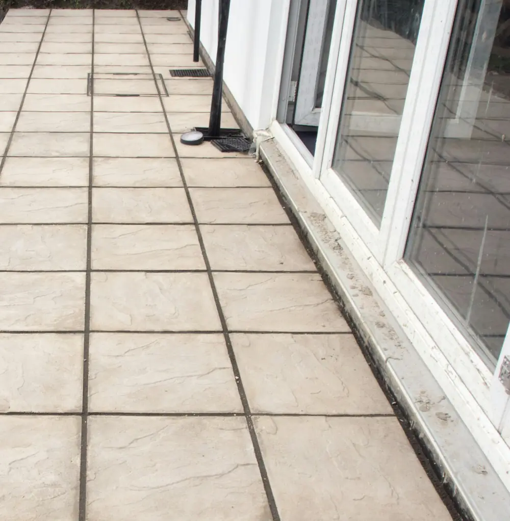 A downspout ending on paving next to a house wall